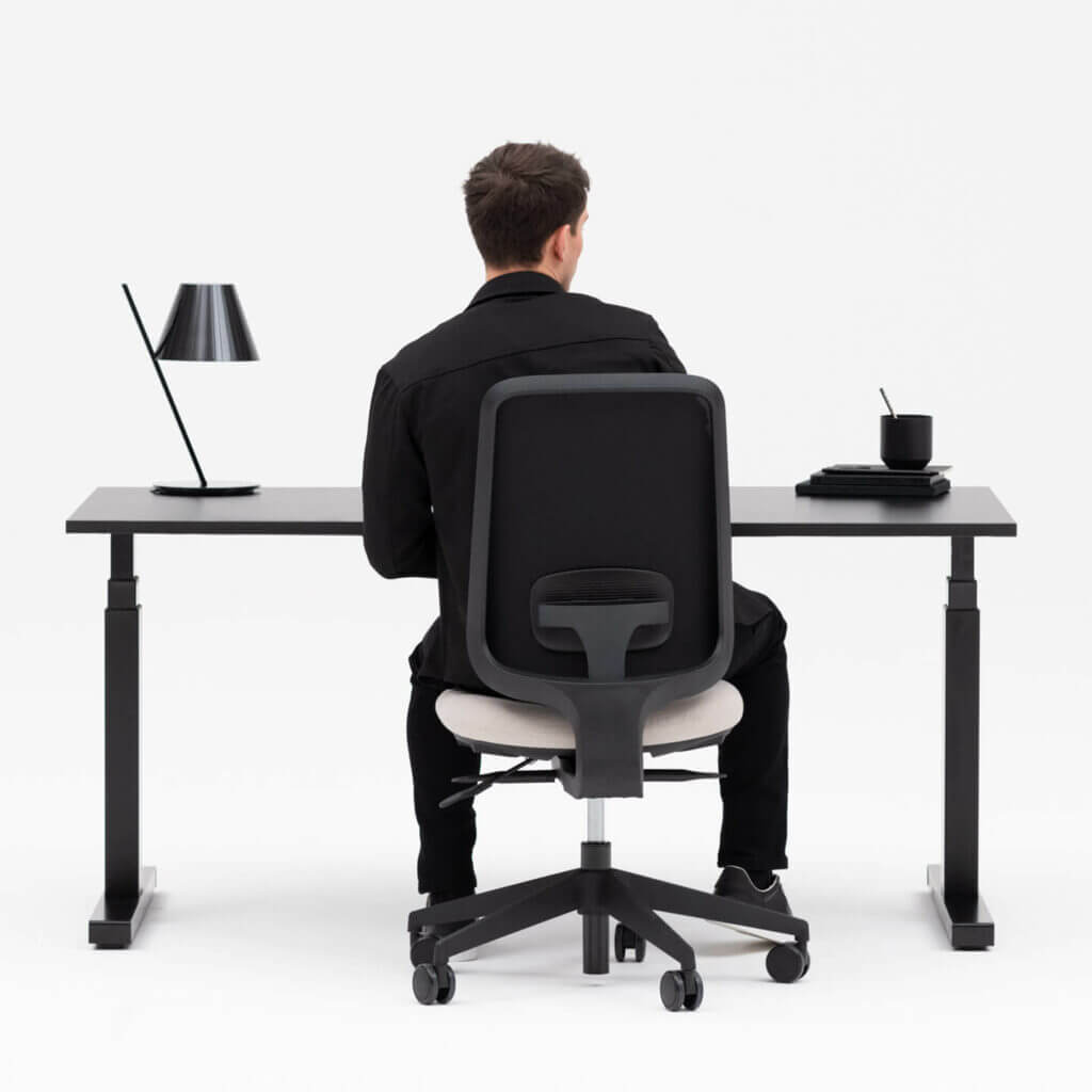 Person Sitting on a Black Frame Office Chair at a Height Adjustable Black Frame Desk