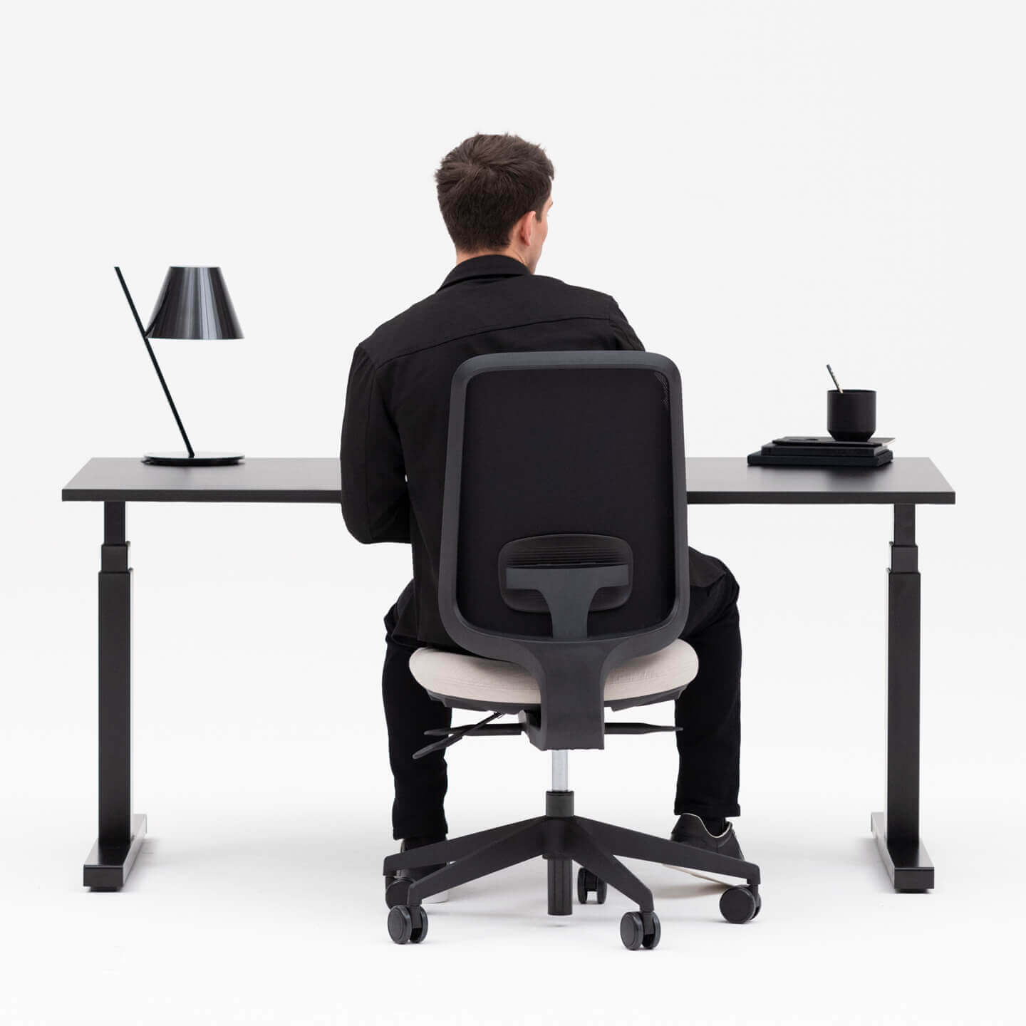Person Sitting on a Black Frame Office Chair at a Height Adjustable Black Frame Desk