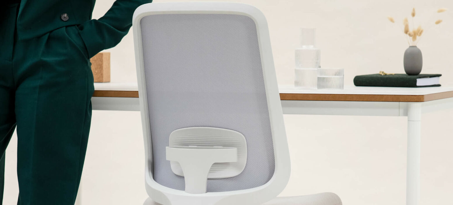 Close Up Of A Task One Office Chair At A Workstation With A Model Wearing An Emerald Green Suit Stood Next To It