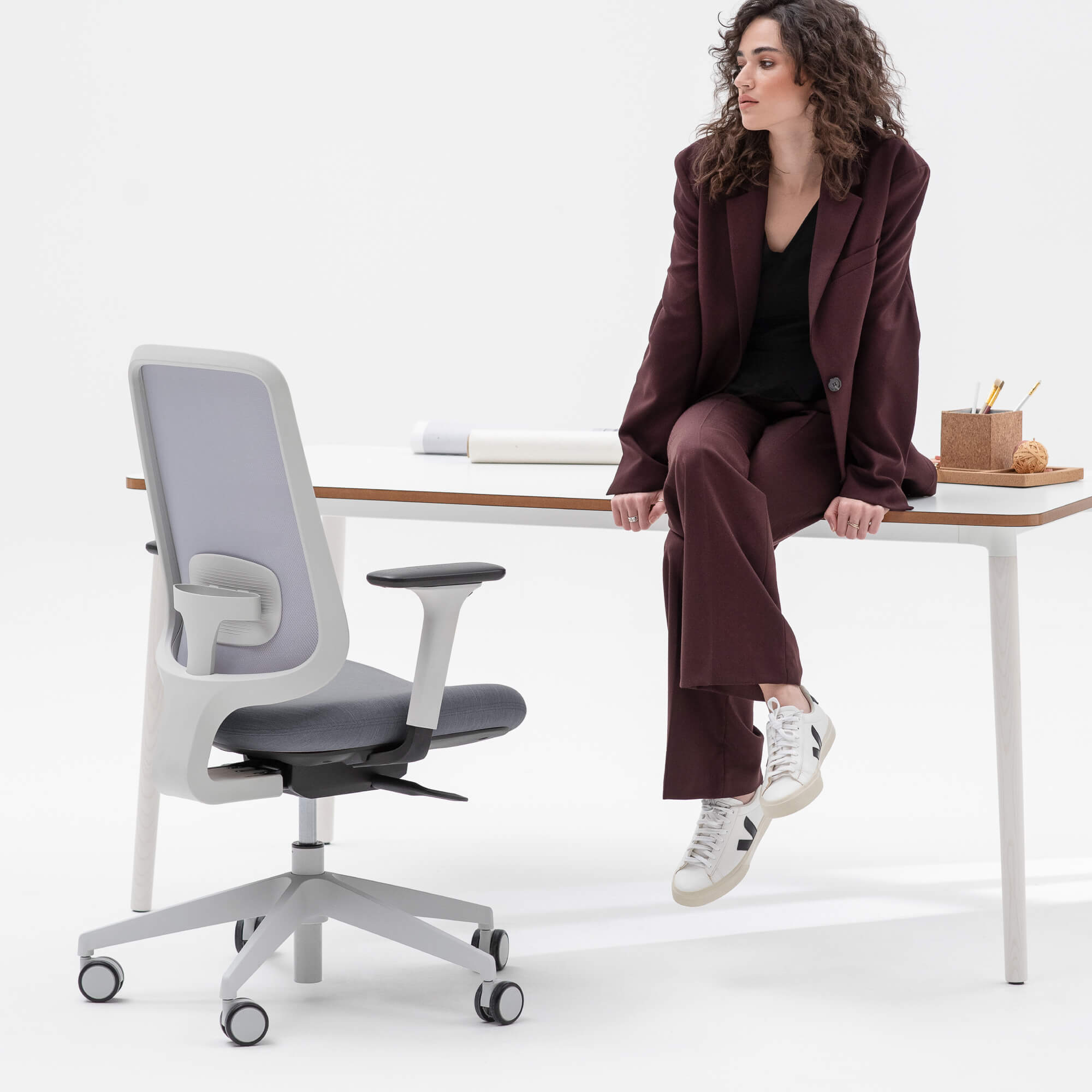 Person Sitting On The Edge Of A Workstation With Their Legs Crossed And A Task One Office Chair Next To Them