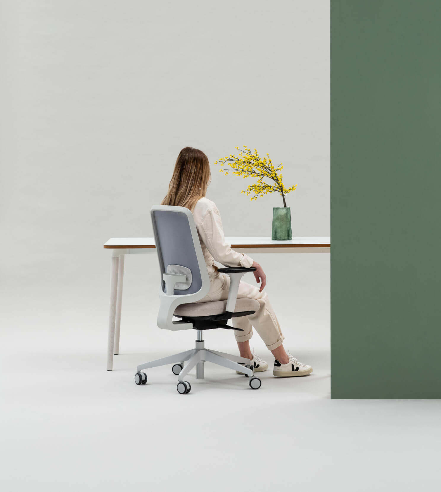The Back Of A Person Sitting On A Task One Grey Frame Office Chair At A Workstation