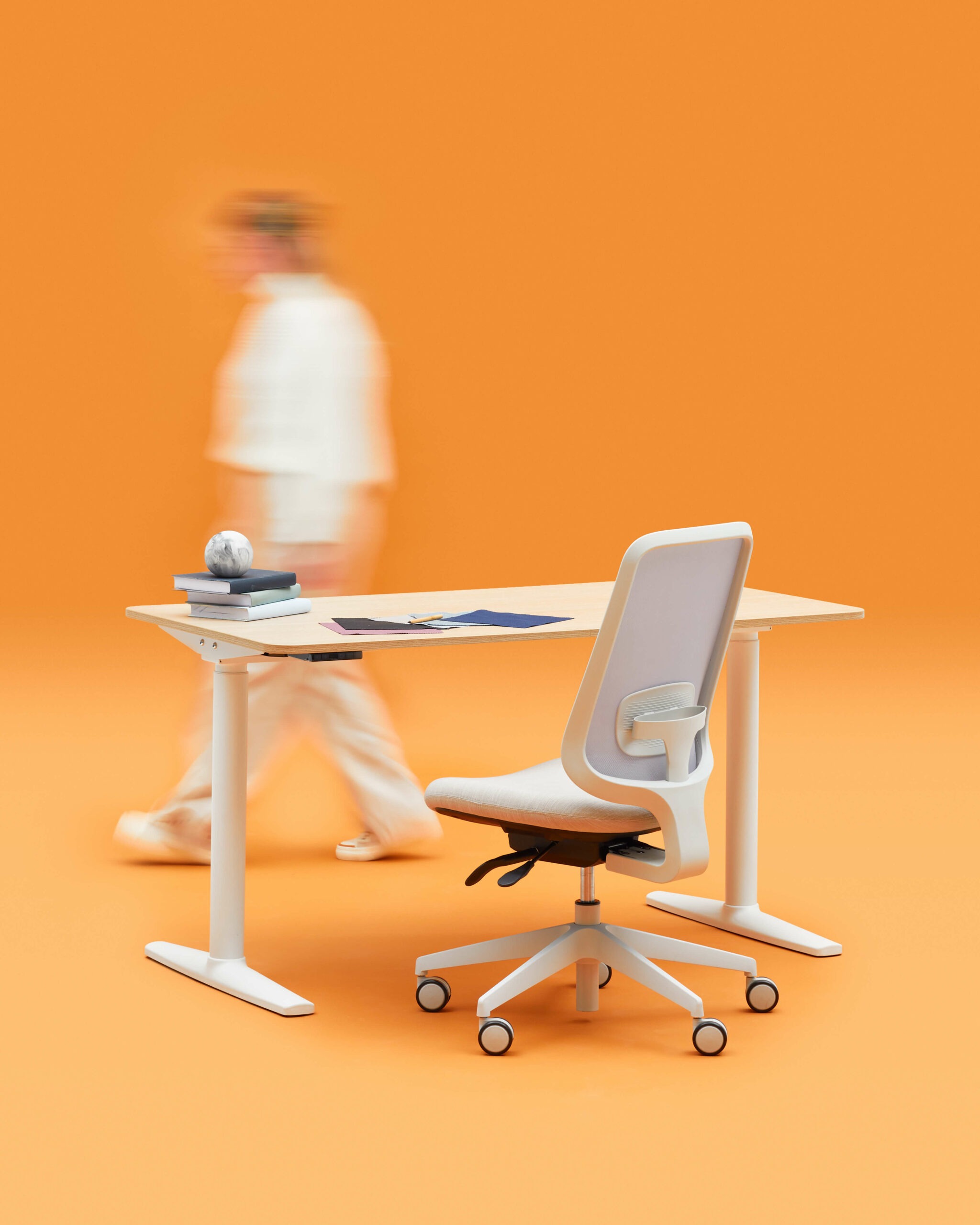 Blurred Person Walking In Front Of A Desk One Adjustable Height Desk And An Armless Task One Office Chair