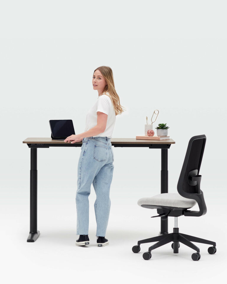 Person Standing In Front Of a Height Adjustable Black Frame Desk Rotating Towards You