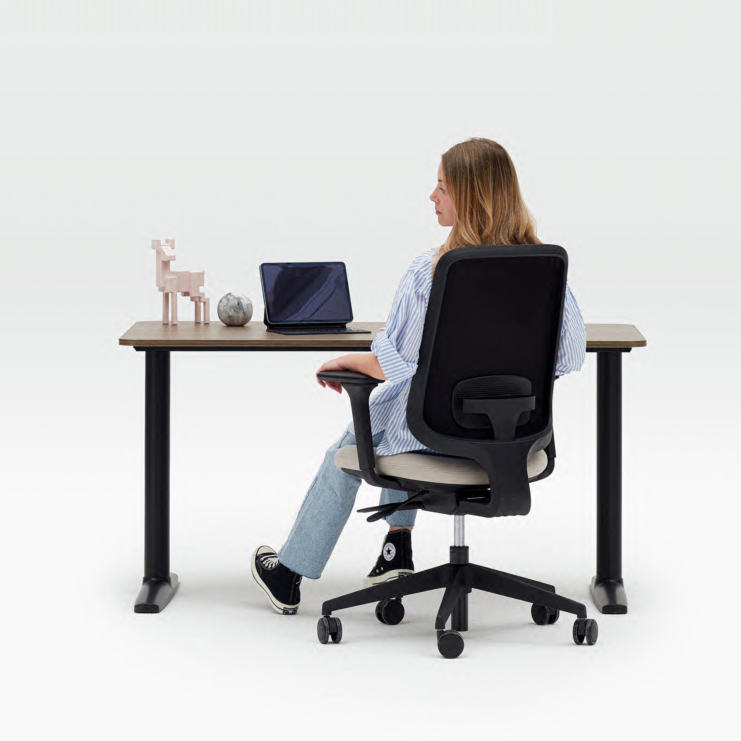 The Back Of A Person Sitting On A Task One Office Chair At A Fixed Height Desk With Their Laptop And Accessories On It