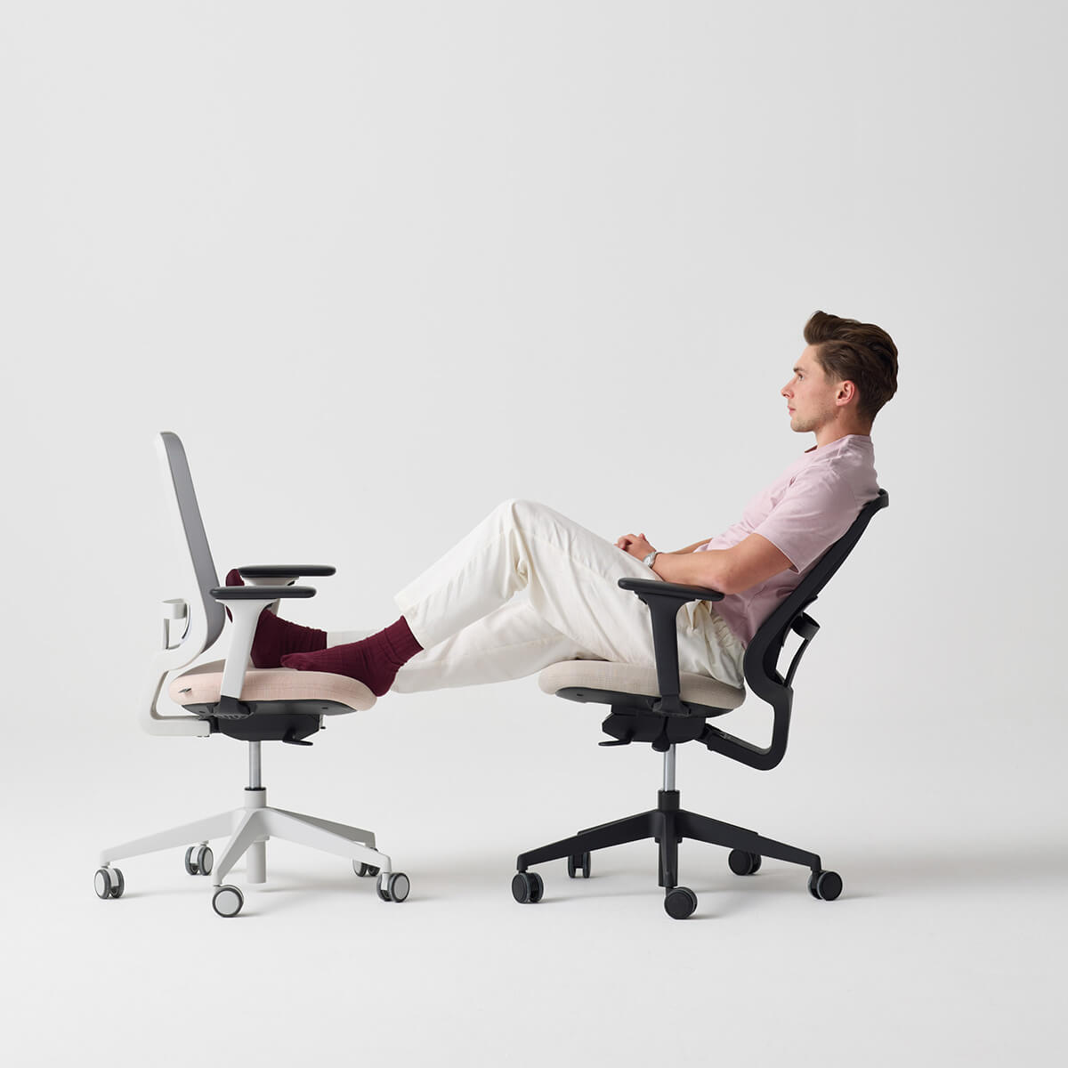 A model sat on a slouch office chair with his legs resting on a second slouch office chair